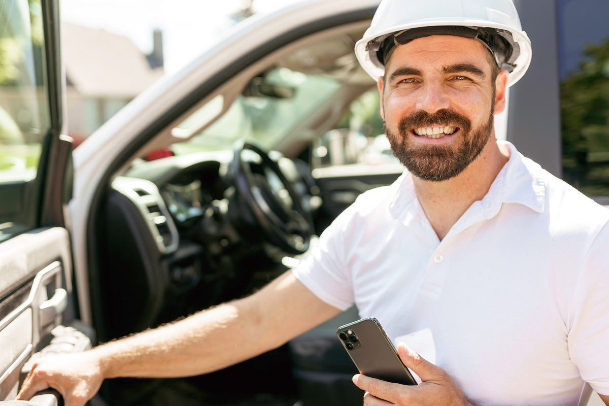 A Man engineer builder wearing a white hard hat, shirt in front of his pickup using cellphone